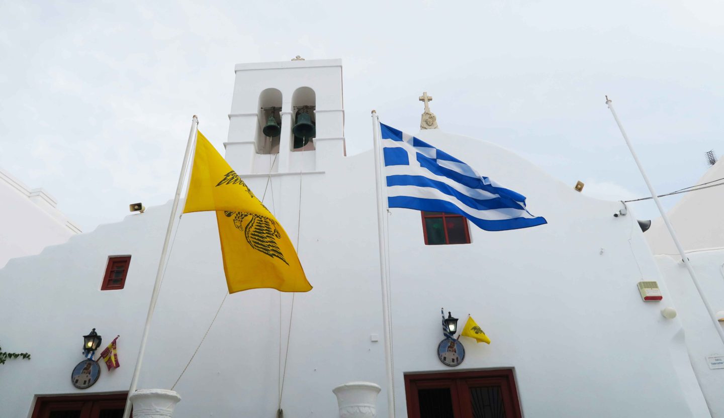 white church in mykonos town with greek flag