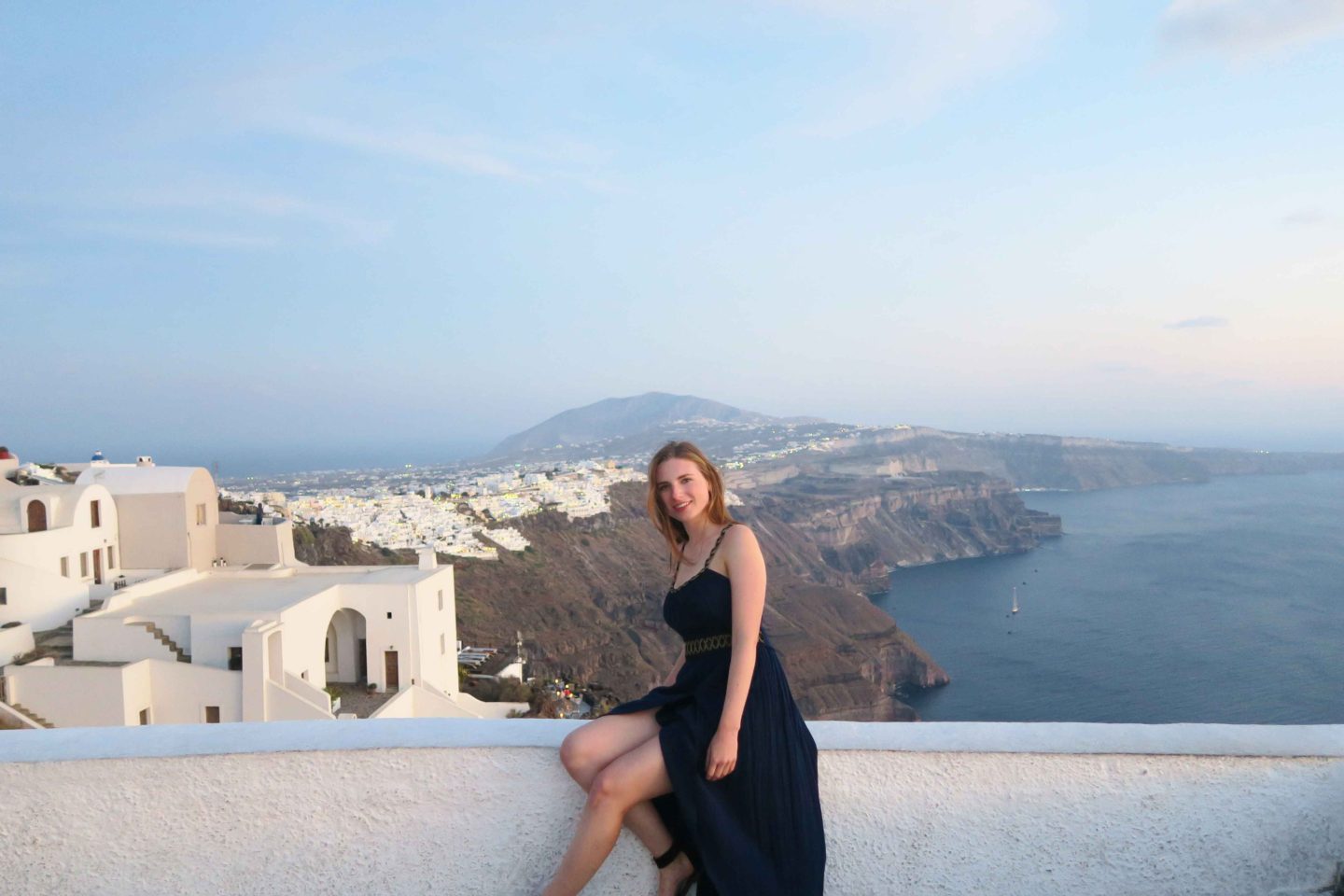 melissa carne in greek dress sitting on white wall in santorini greece