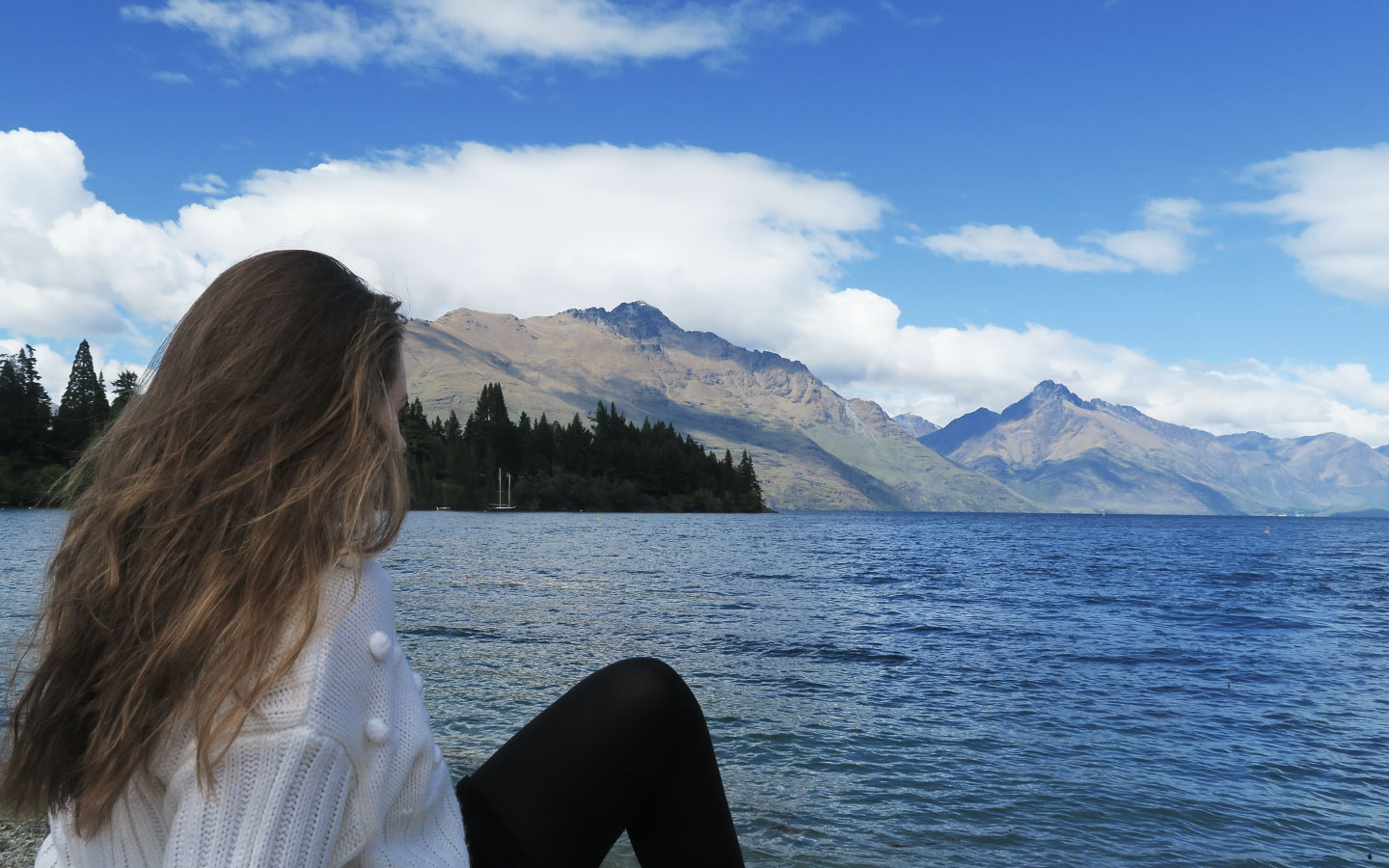 meliss carne sitting in front of mountains and lake wakatipu in new zealand